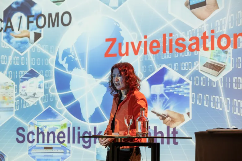 Silvia Ziolkowski auf der Bühne vor der Projektion „Zuvielisation“